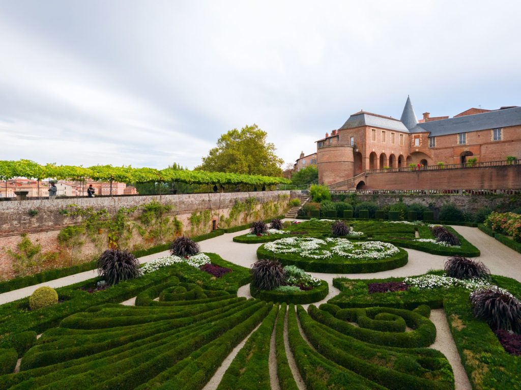 Formaler französischer Garten mit akkurat geschnittenen Hecken und einem Backsteingebäude.