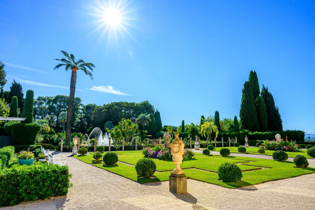 Sonniger formaler Garten mit Skulpturen und gepflegten Hecken.